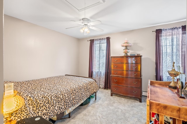 carpeted bedroom with attic access, a baseboard heating unit, and a ceiling fan