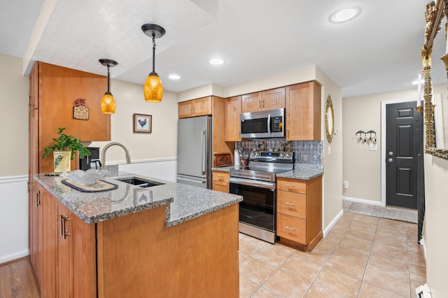 kitchen with backsplash, a sink, stone countertops, a peninsula, and stainless steel appliances