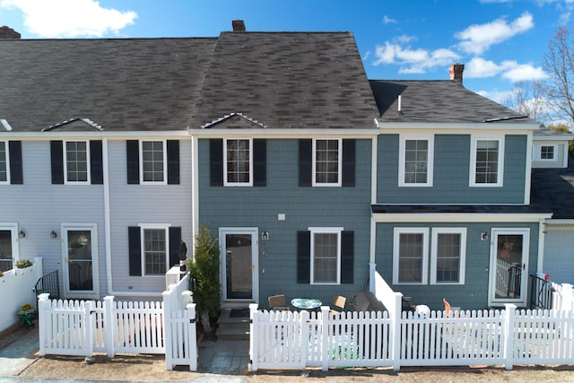 view of front facade featuring a shingled roof, a chimney, and a fenced front yard