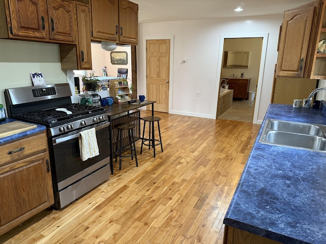 148 Pendleton Point Rd, Islesboro, ME 04848 - kitchen featuring stainless steel gas range oven, a sink, light wood finished floors, dark countertops, and brown cabinetry