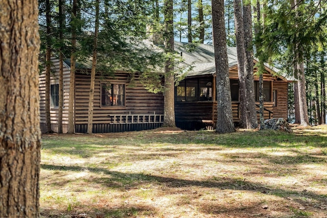 back of house featuring faux log siding, a sunroom, and a shingled roof