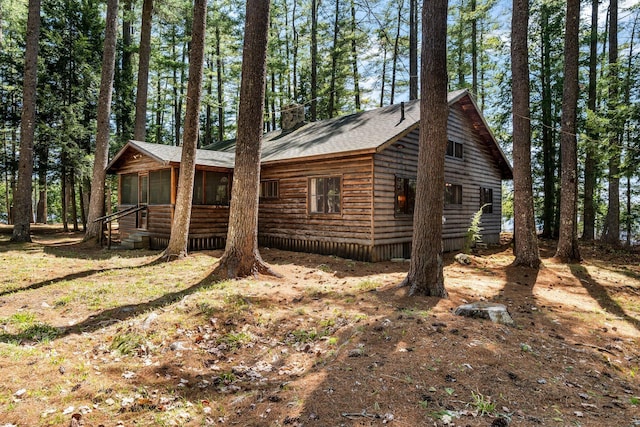 view of side of home featuring a sunroom, a chimney, and a shingled roof