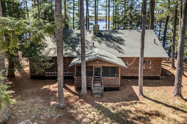 rear view of property with a shingled roof, log veneer siding, and a chimney