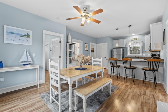 dining area with baseboards, light wood-style floors, and a ceiling fan