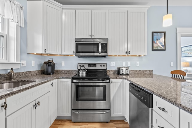 kitchen with a sink, light wood-type flooring, stainless steel appliances, white cabinets, and dark stone counters