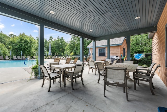 view of patio with a community pool, fence, and outdoor dining space