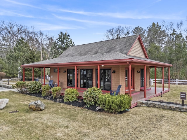 country-style home featuring covered porch, a shingled roof, fence, and a front lawn