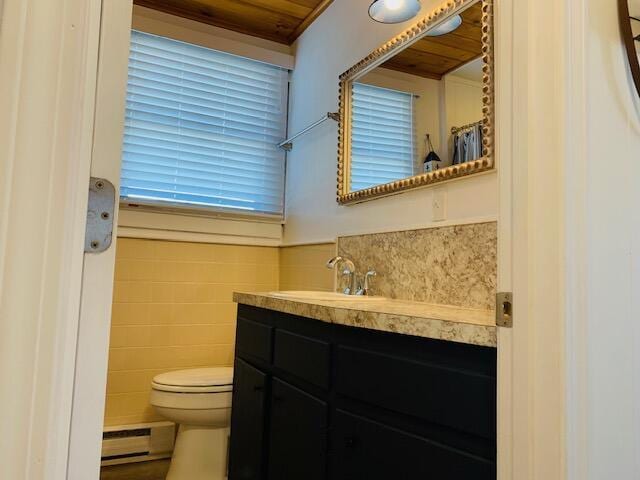 bathroom with vanity, tile walls, a baseboard heating unit, toilet, and wainscoting