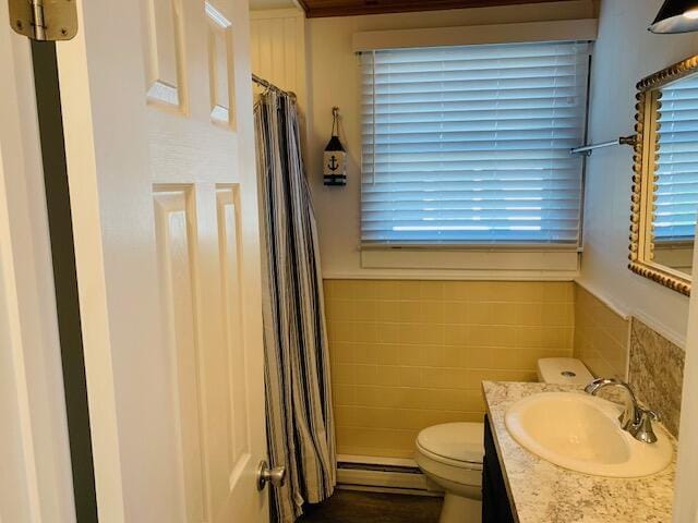 full bathroom featuring toilet, curtained shower, vanity, a baseboard heating unit, and tile walls