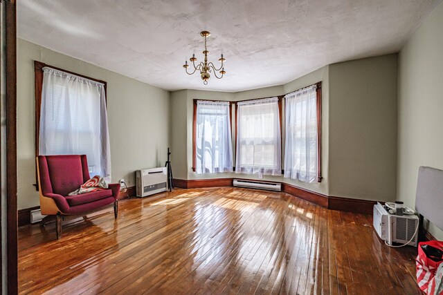 living area with a baseboard heating unit, hardwood / wood-style floors, a chandelier, and baseboards