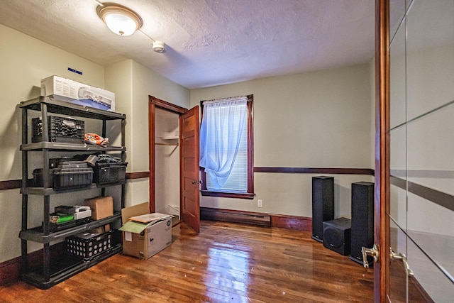 interior space with wood finished floors, a baseboard radiator, a textured ceiling, and baseboards