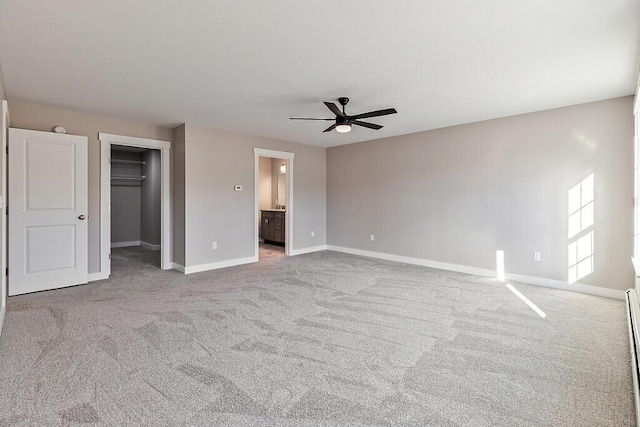 unfurnished bedroom with a spacious closet, carpet, baseboards, ensuite bath, and a ceiling fan