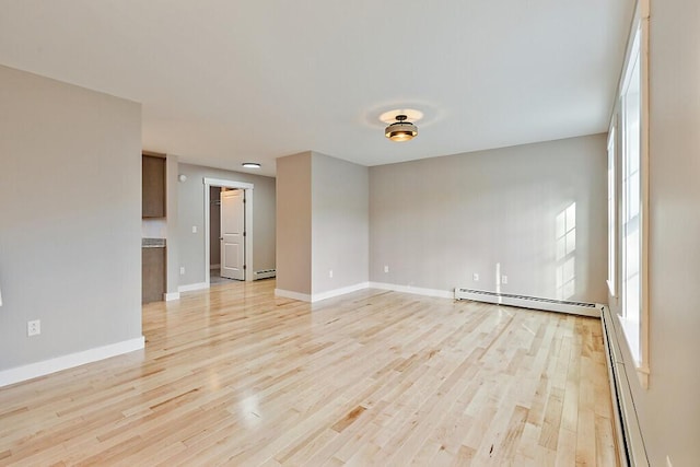 empty room featuring a baseboard radiator, light wood-style flooring, baseboards, and a wealth of natural light