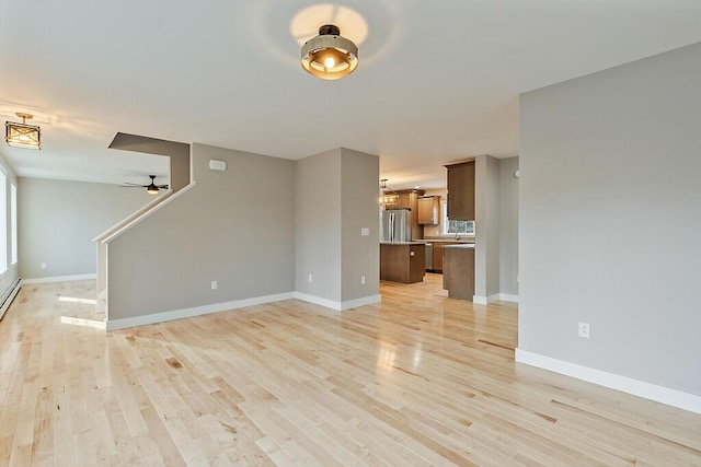 unfurnished living room with baseboards, ceiling fan, stairway, and light wood finished floors