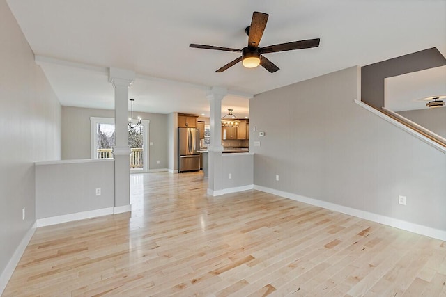 unfurnished living room with ceiling fan with notable chandelier, decorative columns, light wood-style floors, and baseboards