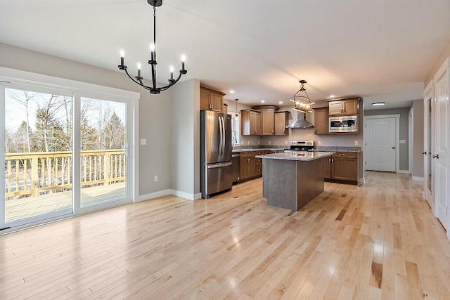 kitchen featuring a notable chandelier, wall chimney exhaust hood, a center island, light wood-style flooring, and stainless steel appliances