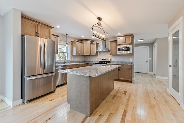 kitchen featuring stainless steel appliances, light stone counters, light wood finished floors, and wall chimney exhaust hood