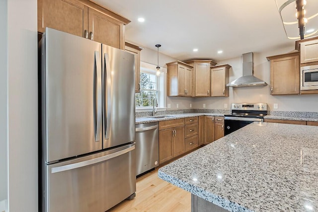 kitchen featuring light stone counters, a sink, stainless steel appliances, wall chimney range hood, and light wood-style floors