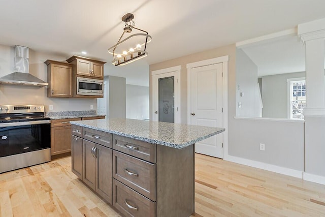 kitchen featuring stainless steel appliances, baseboards, light wood finished floors, light stone countertops, and wall chimney exhaust hood