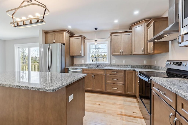 kitchen with light stone counters, a sink, wall chimney exhaust hood, stainless steel appliances, and light wood-style floors