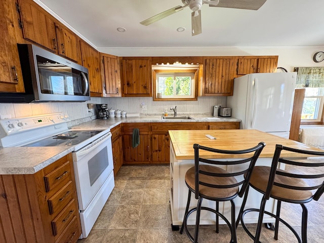 kitchen featuring a sink, ceiling fan, brown cabinets, and white appliances