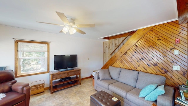 living area featuring wooden walls, baseboards, and a ceiling fan
