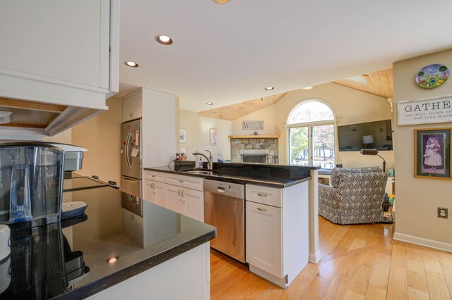 kitchen with white cabinets, a sink, stainless steel appliances, open floor plan, and a fireplace