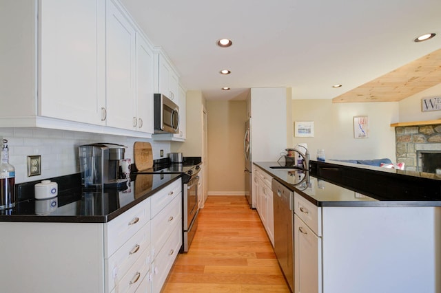 kitchen with recessed lighting, appliances with stainless steel finishes, white cabinets, a sink, and a peninsula