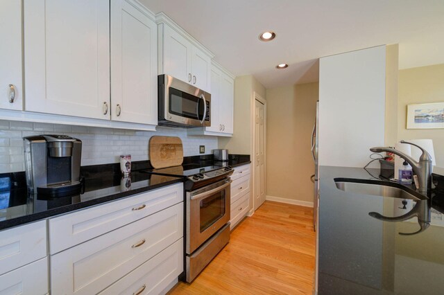 kitchen with a sink, stainless steel appliances, light wood-style floors, backsplash, and white cabinets