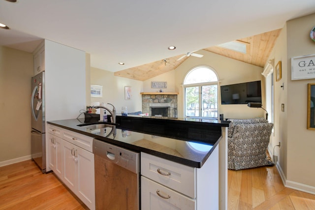 kitchen featuring a peninsula, appliances with stainless steel finishes, dark countertops, a sink, and open floor plan
