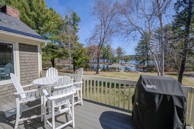 deck with outdoor dining space, a yard, a water view, and a grill
