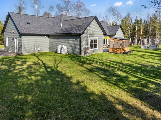 rear view of property with roof with shingles and a yard