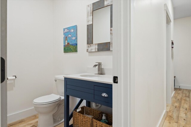 half bath with toilet, wood finished floors, baseboards, and vanity
