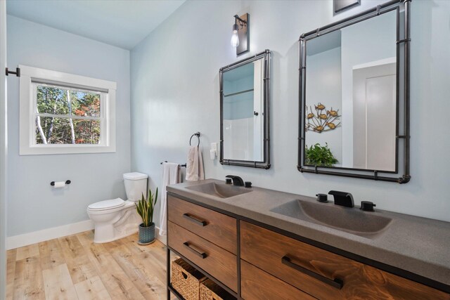 full bath featuring toilet, baseboards, wood finished floors, and double vanity
