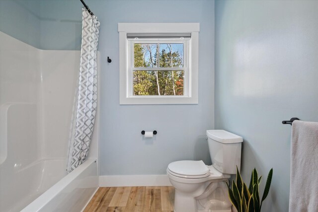 full bath featuring toilet, baseboards, wood finished floors, and shower / tub combo