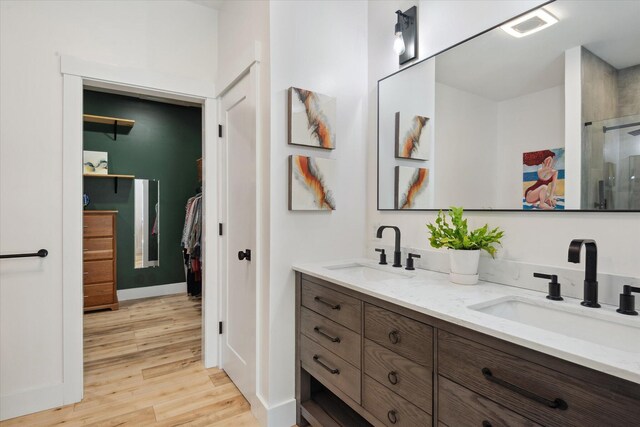 bathroom featuring wood finished floors, double vanity, a walk in closet, and a shower