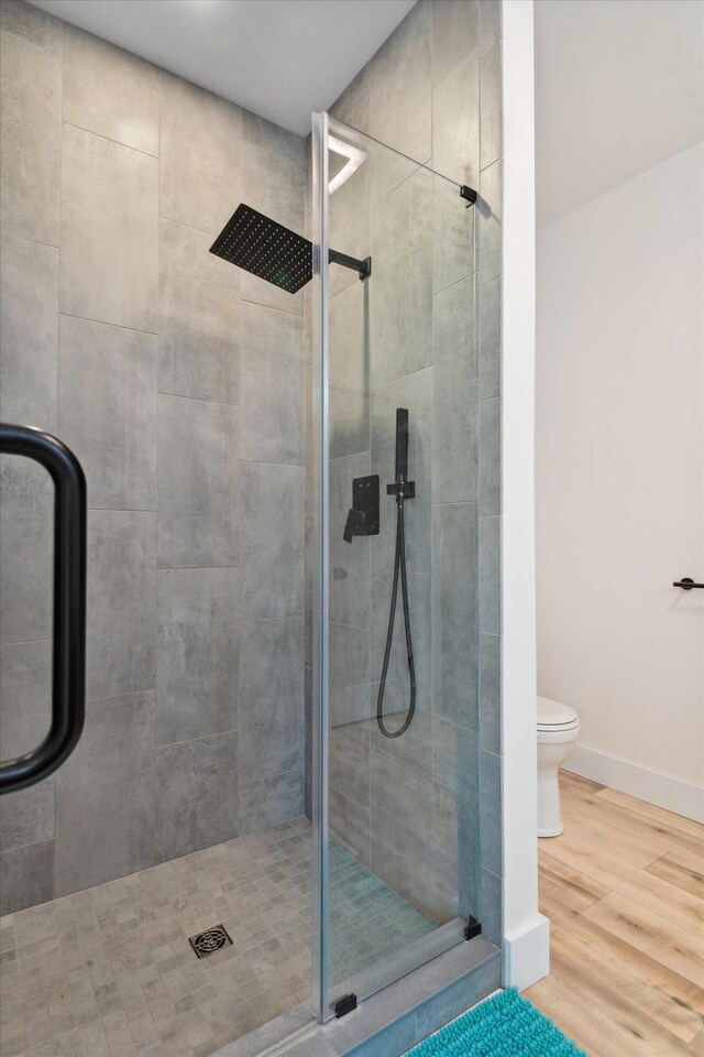 full bathroom with a stall shower, wood finished floors, baseboards, and toilet