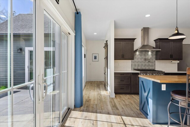 kitchen featuring wall chimney range hood, butcher block countertops, dark brown cabinets, and recessed lighting