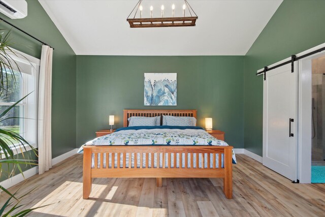 bedroom with a barn door, lofted ceiling, wood finished floors, and baseboards