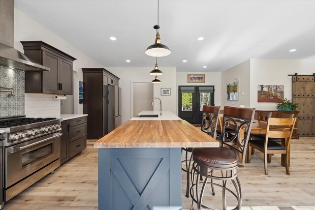 kitchen with appliances with stainless steel finishes, wall chimney exhaust hood, a sink, light wood-style floors, and recessed lighting