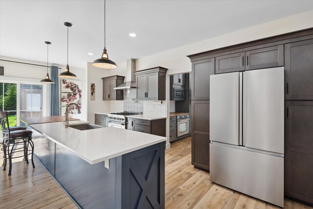 kitchen featuring stainless steel appliances, a sink, wall chimney range hood, backsplash, and recessed lighting