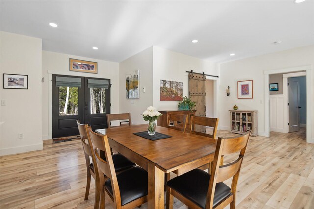 dining area with a barn door, light wood-style flooring, french doors, recessed lighting, and baseboards