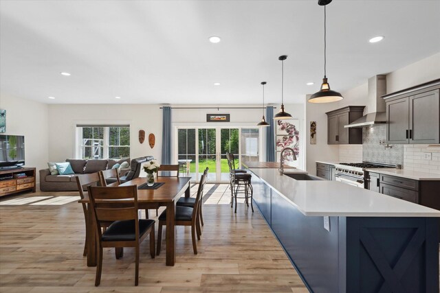 kitchen with wall chimney range hood, high end range, a sink, recessed lighting, and light wood finished floors