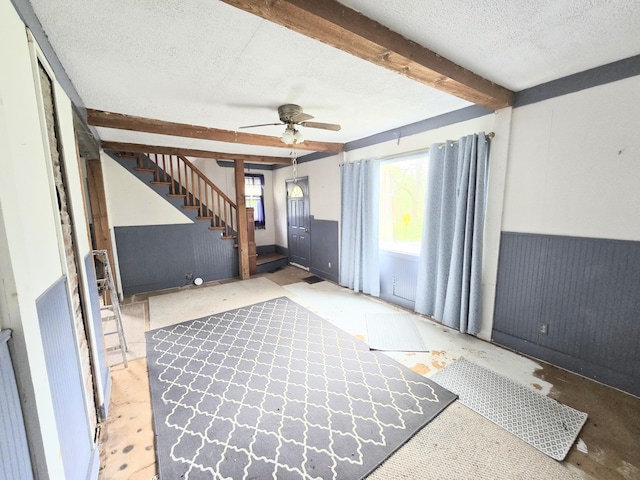 27 Cannard St, Gardiner, ME 04345 - unfurnished living room with beamed ceiling, a textured ceiling, a ceiling fan, stairway, and wainscoting