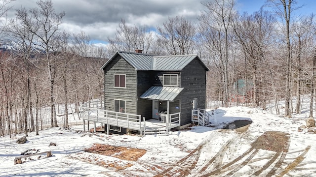 snow covered property featuring a deck, a standing seam roof, a chimney, and metal roof
