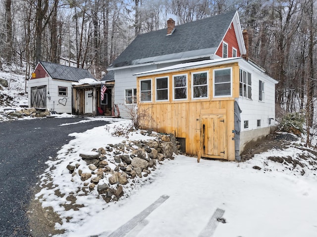 rustic home with a garage, an outbuilding, a shingled roof, and a chimney