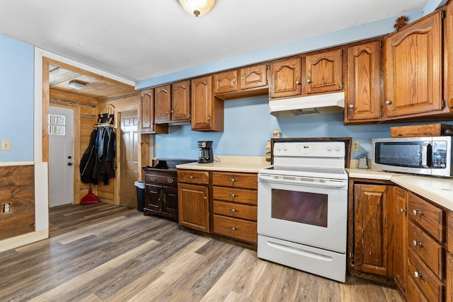 kitchen with light wood-type flooring, brown cabinetry, under cabinet range hood, stainless steel microwave, and electric range