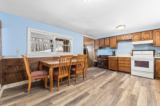 kitchen with light countertops, brown cabinets, light wood-style flooring, under cabinet range hood, and electric stove