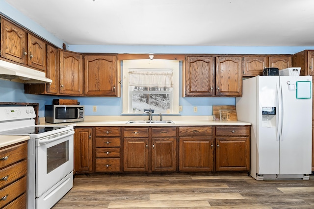 kitchen with light countertops, white appliances, dark wood-type flooring, under cabinet range hood, and a sink