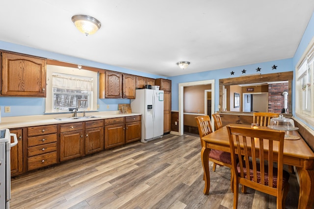 kitchen with light countertops, a sink, white refrigerator with ice dispenser, brown cabinets, and light wood-type flooring
